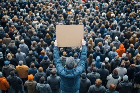 Fotografía aérea de una manifestación ciudadana en invierno con cientos de personas congregadas y, en primer plano, un manifestante de espaldas sosteniendo una pancarta en blanco.