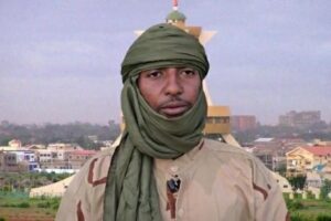 Retrato de Jafar Dicko, líder de Ansarul Islam, con turbante verde, en un entorno urbano al fondo